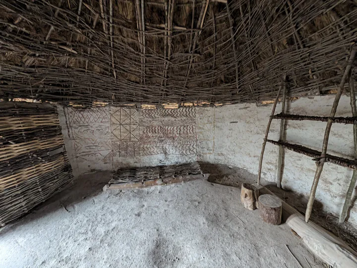The inside of a reconstructed hut. There are paintings on the walls.
