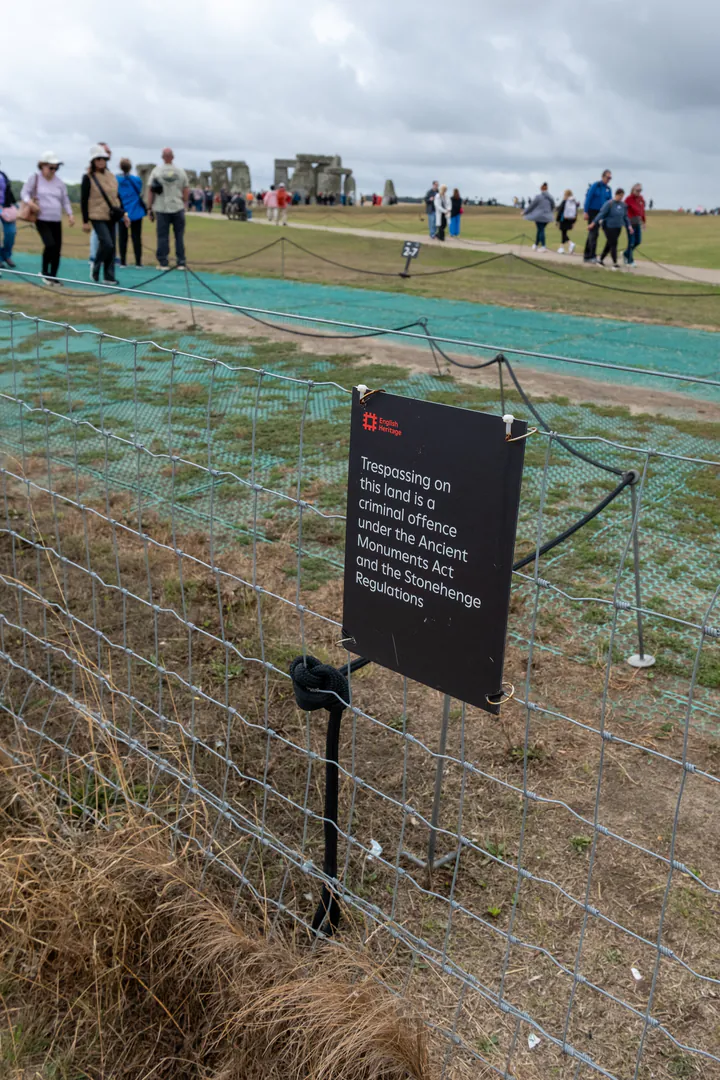 A sign on the Stonehenge free footpath telling people not to trespass. The stone circle is in the background.