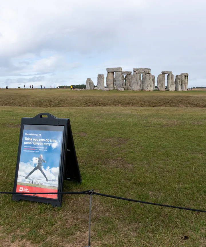 A sign suggesting funny photos that visitors can take, with Stonehenge in the background