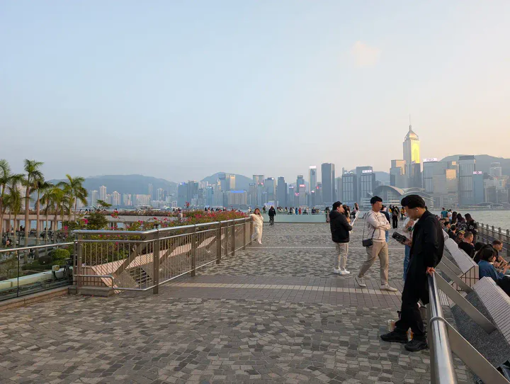 A wide pedestrian walkway beside Hong Kong's famous harbour, with skyscrapers in the background.