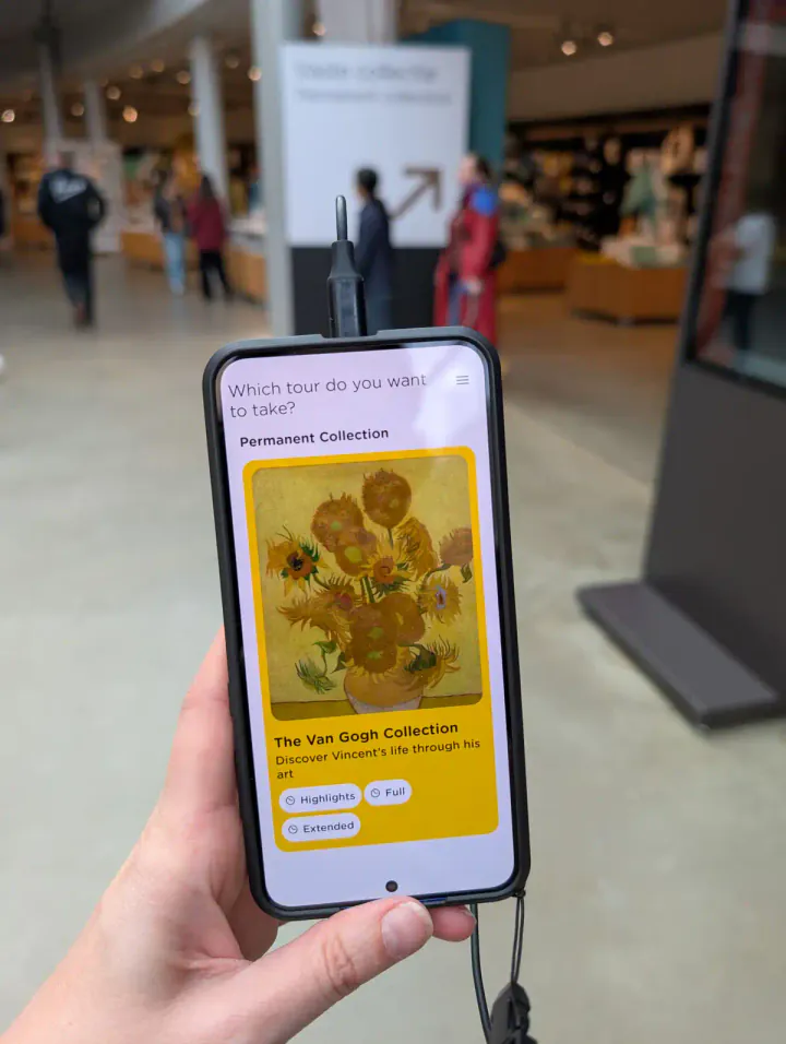 A hand holding what looks like a mobile phone, with an audio guide on the screen