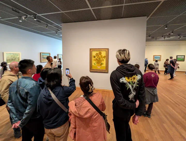 People crowded around Van Gogh's Sunflowers painting in the museum in Amsterdam