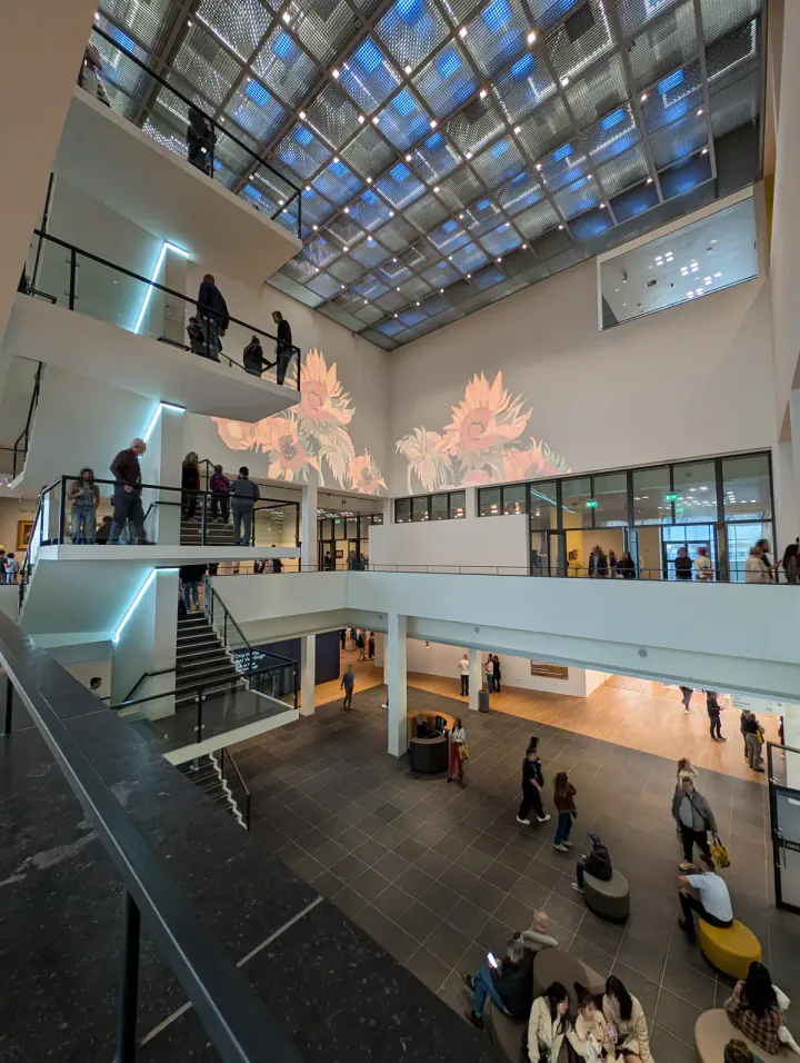 The atrium of the Van Gogh Museum, Amsterdam. There are four floors, with staircases between them. A image of Van Gogh's Sunflowers is being projected on the wall.