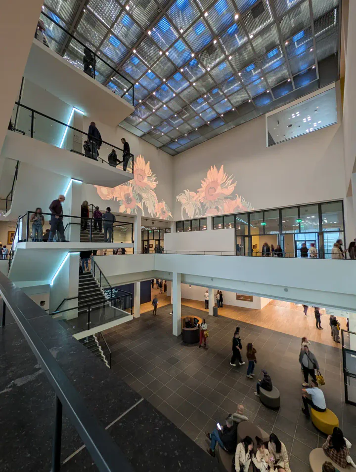 The atrium of the Van Gogh Museum, Amsterdam. There are four floors, with staircases between them. A image of Van Gogh's Sunflowers is being projected on the wall.