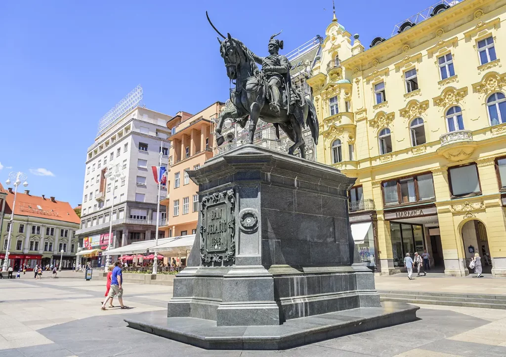 Ban Jelačić Square in Zagreb, Croatia. A large statue of a man on horseback is in the middle of a European city square with brightly coloured and ornately decorated buildings. 