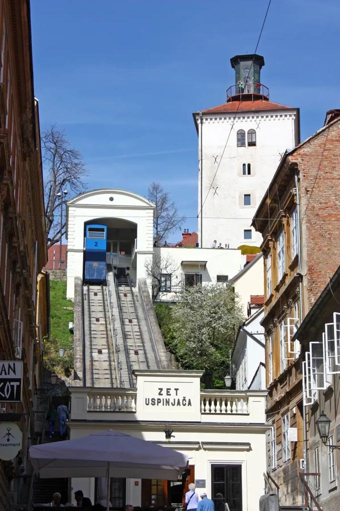The Lotrščak Tower and funicular railway between Zagreb's upper and lower town. A white, medieval, fortified tower stands at the top of a hill, with a 19th century funicular railway running up the hill.