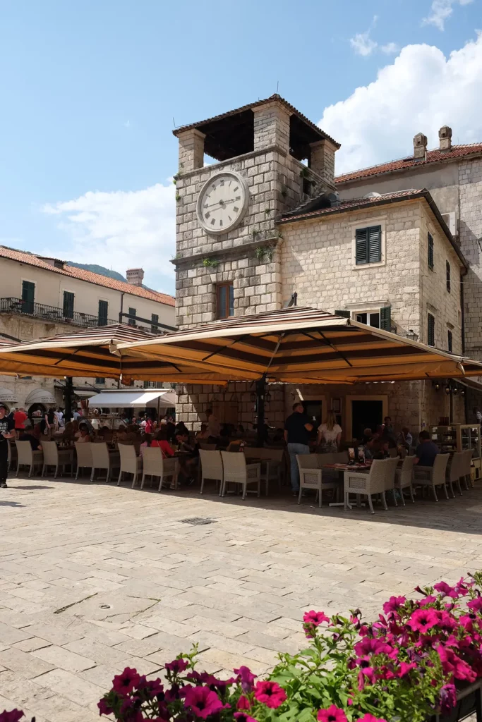 The square in the middle of Kotor, with people at tables underneath an old stone clock tower