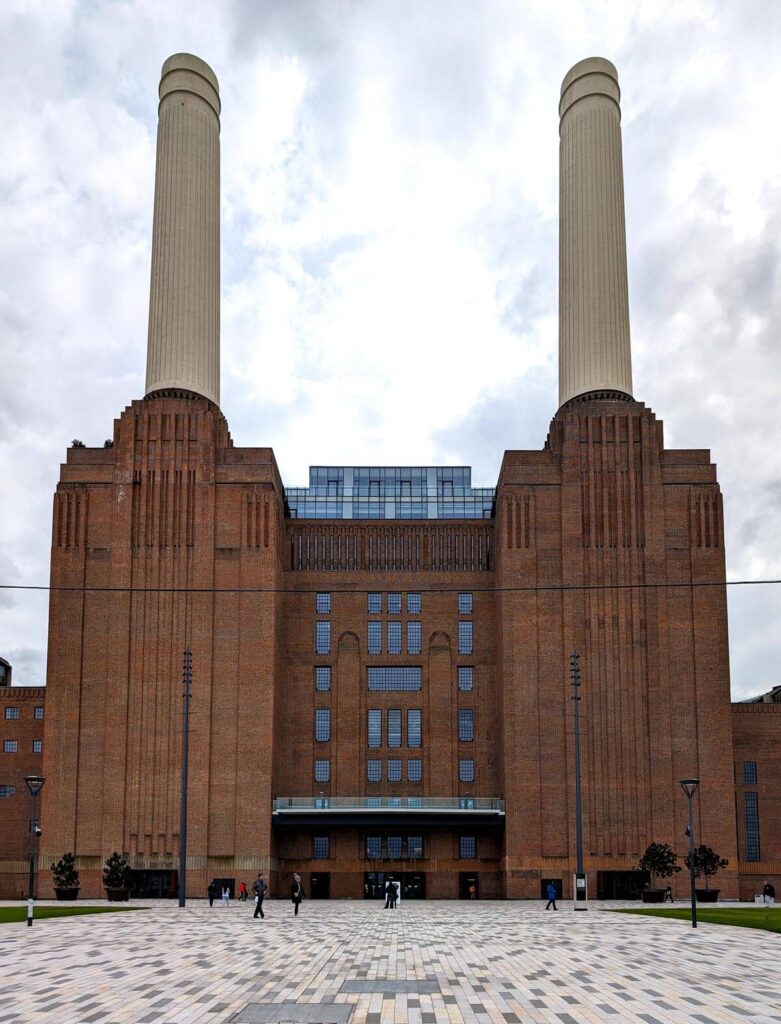 The front of Battersea Power Station in London. A large, Art Deco, industrial building built of brick. The building is very symmetrical, two of the four white towers are visible.