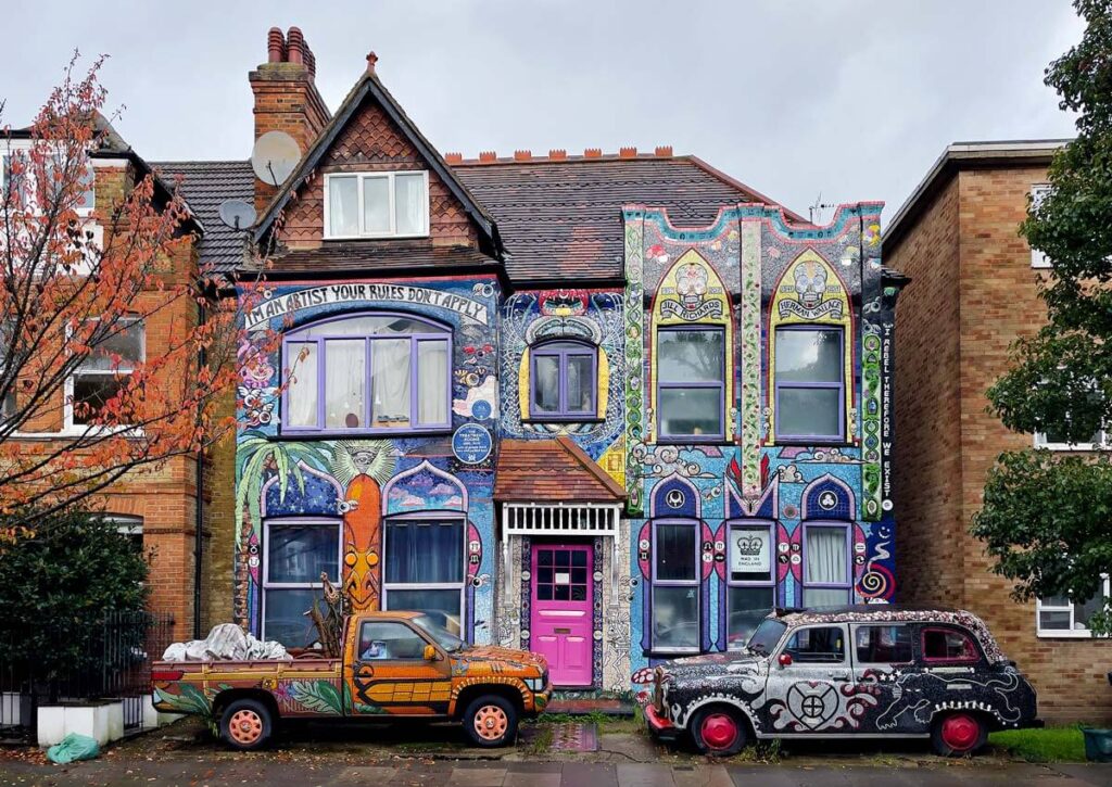 The mosaic house in London. A normal red brick London semi-detatched house is covered in intricate mosaics. There are two cars covered in mosaics in the front yard. 