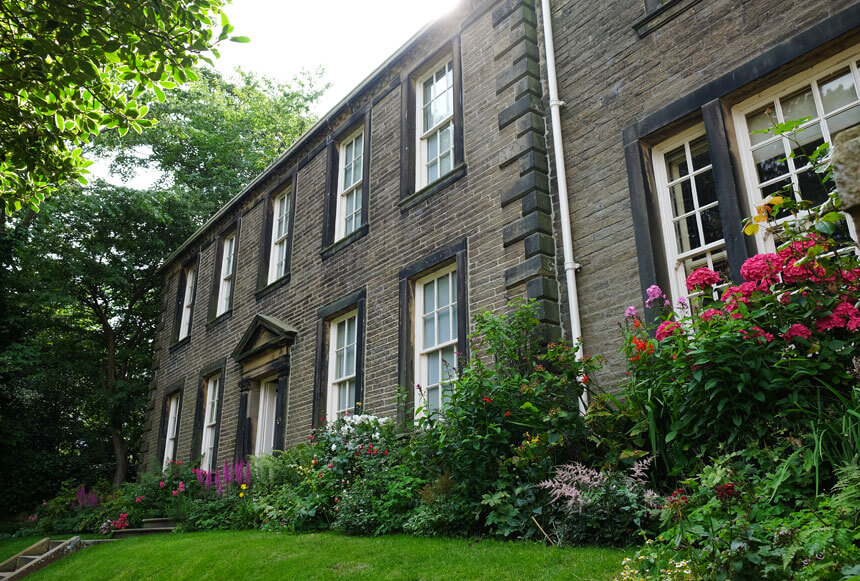 The Brontë Parsonage Museum in Haworth celebrates the life of Charlotte, Emily and Anne Brontë. A stone house with large windows sits in a beautiful cottage garden with lots of flowers. 