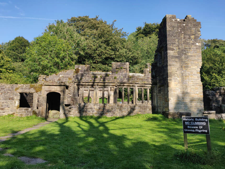 The ruins of Wycoller Hall, which inspired Charlotte Brontë. A ruined stone house with mullioned windows and a tower sits on a green grass lawn.