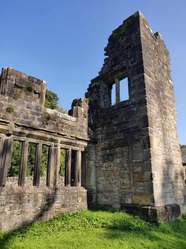 The ruins of the tower at Wycoller Hall. A jagged, crumbling tower is the highest point of once-grand Wycoller Hall. Plants are growing out of the wall and any glass in the windows has long-since disappeared. 
