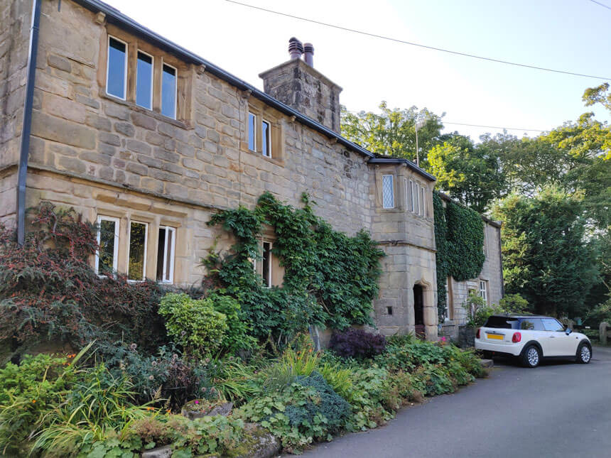 Only residents' cars are allowed in the village. A white car is parked in front of an old stone house with an arched doorway and partly covered with ivy. 