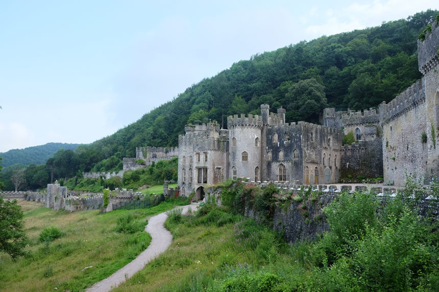 Gwrych Castle in Abergele, North Wales. A large, long castle with towers and castellated walls is set into a Welsh hillside.