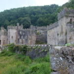 The outside of Gwrych Castle in North Wales. A ruined, roofless but very grand castle in grey stone with gothic towers spreads across a forested Welsh hillside.