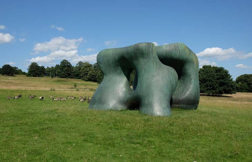 Henry Moore's bronze Two Large Forms. Two greeny-coloured, large bronze sculptures are set in a rolling landscape at the Yorkshire Sculpture Park. A flock of Canada geese are enjoying eating the grass next to the sculpture.