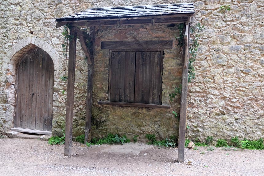 The Ye Olde Shoppe from I'm A Celeb at Grywch Castle. A wooden hatch is in a stone wall with a rickety roof over the top.