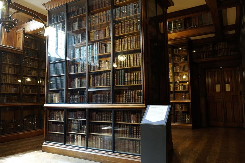 The Spencer Room at the John Rylands Library. Dark wood bookshelves are filled with old, leather-bound books up to the ceiling.