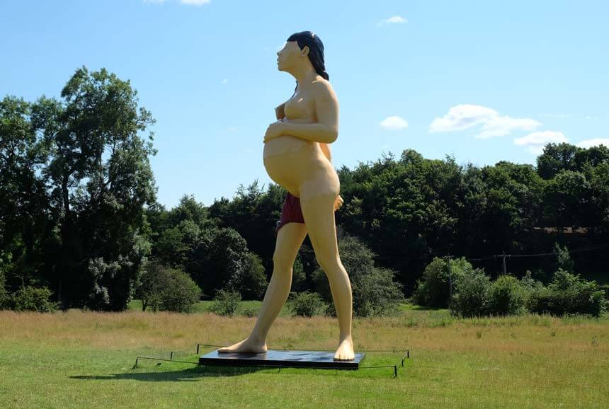 Damien Hirst's The Virgin Mother at Yorkshire Sculpture Park. A very tall sculpture of a pregnant young woman stands in a parkland landscape. You can just see that the skin on one of her legs has been peeled away; the other side of the sculpture shows the foetus inside her. 