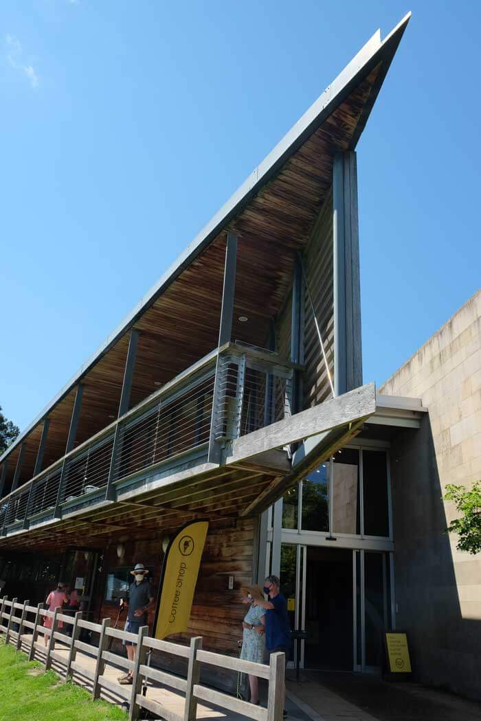 The dramatic lines of Yorkshire Sculpture Park's YSP centre. A modern building with wooden walls and a metal balcony. The roof narrows to a sharp point.