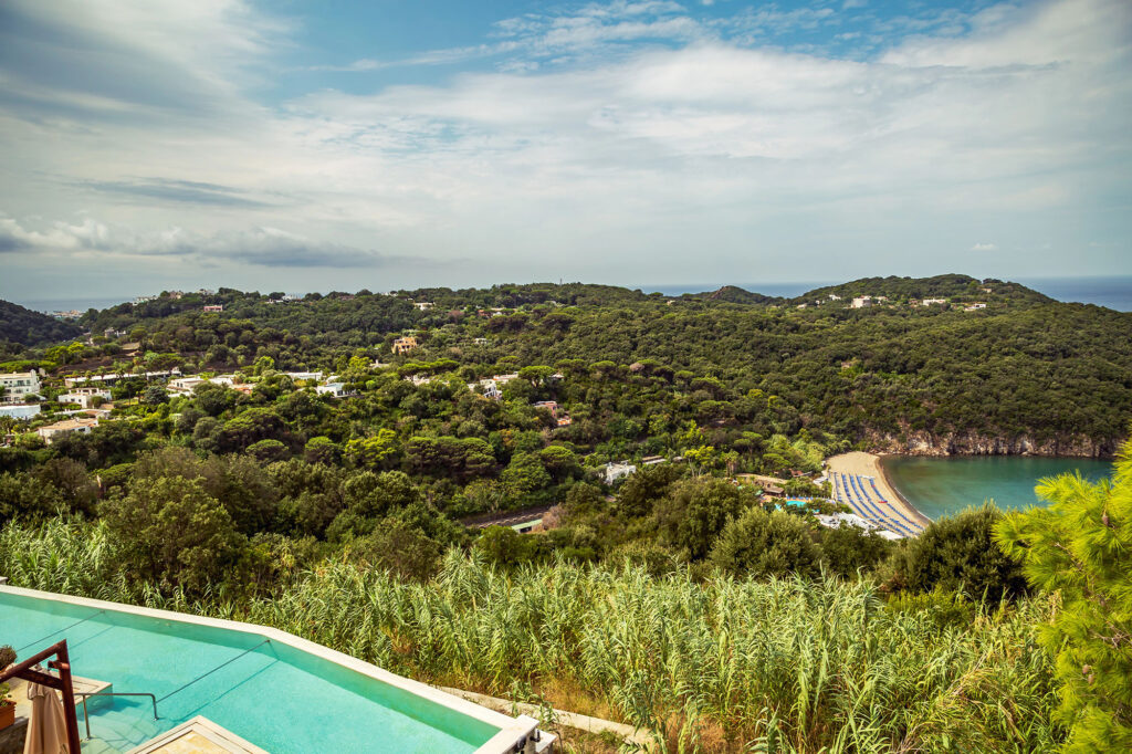 A view of a sandy beach, taken from up on a hill, with a swimming pool in the foreground