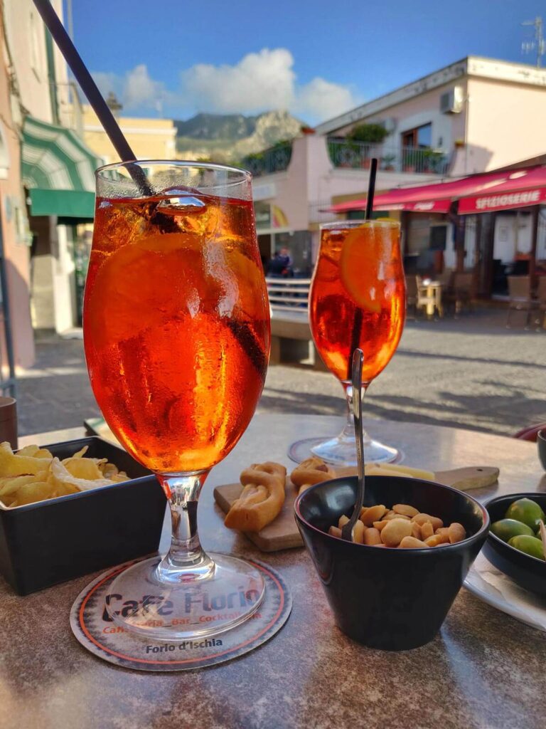a two glasses of orange liquid with a straw next to a bowl of snacks