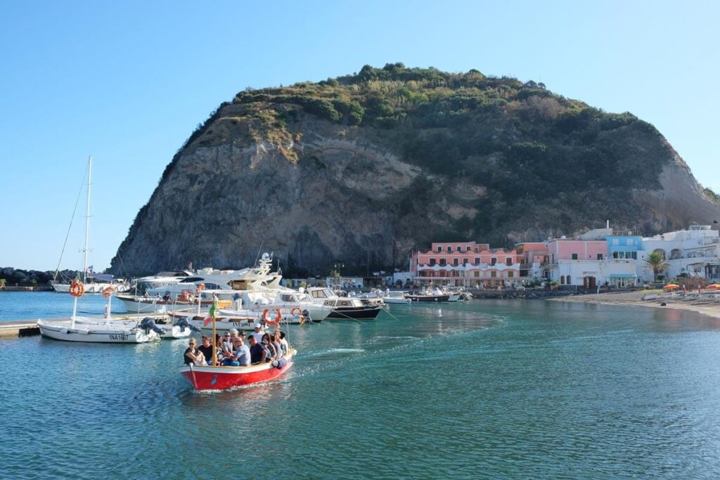 a group of people in a boat in the water with a hill in the background