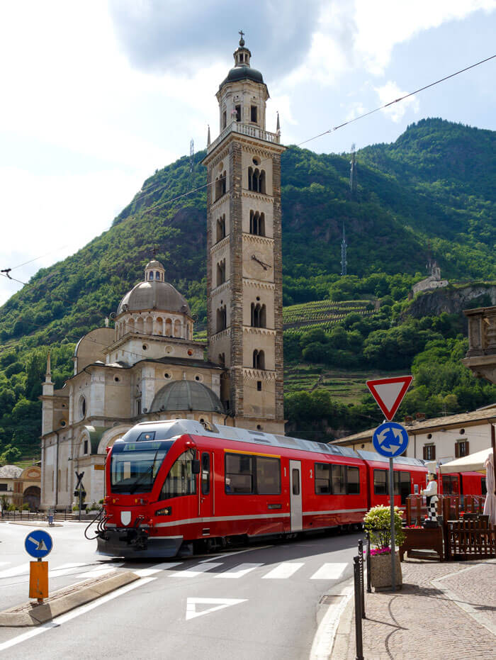 A Bernina Line train passing in front of Tirano's historic church