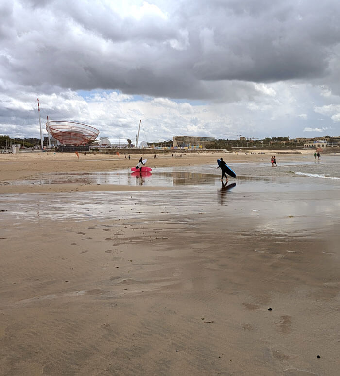 Surfers on the beach, with the She Changes sculpture in the background