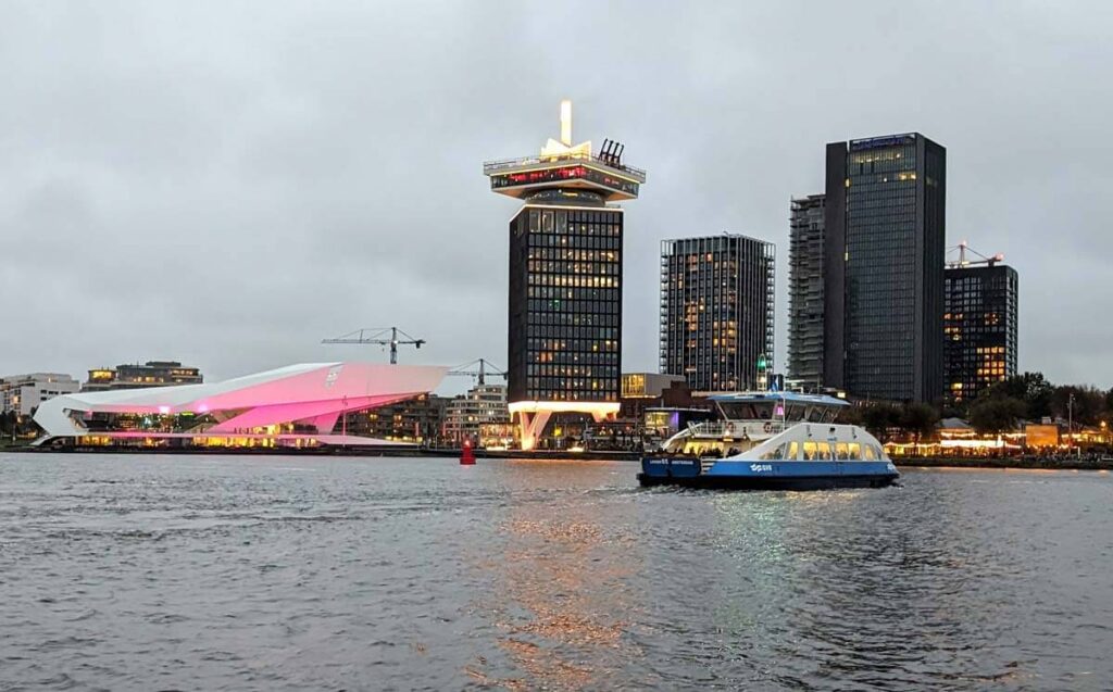 The north bank of the IJ in the early evening. The Eye Filmmuseum is lit up in pink for Museumnacht Amsterdam. The tall building next door has A'DAM Lookout at the top, along with the Over the Edge swing.