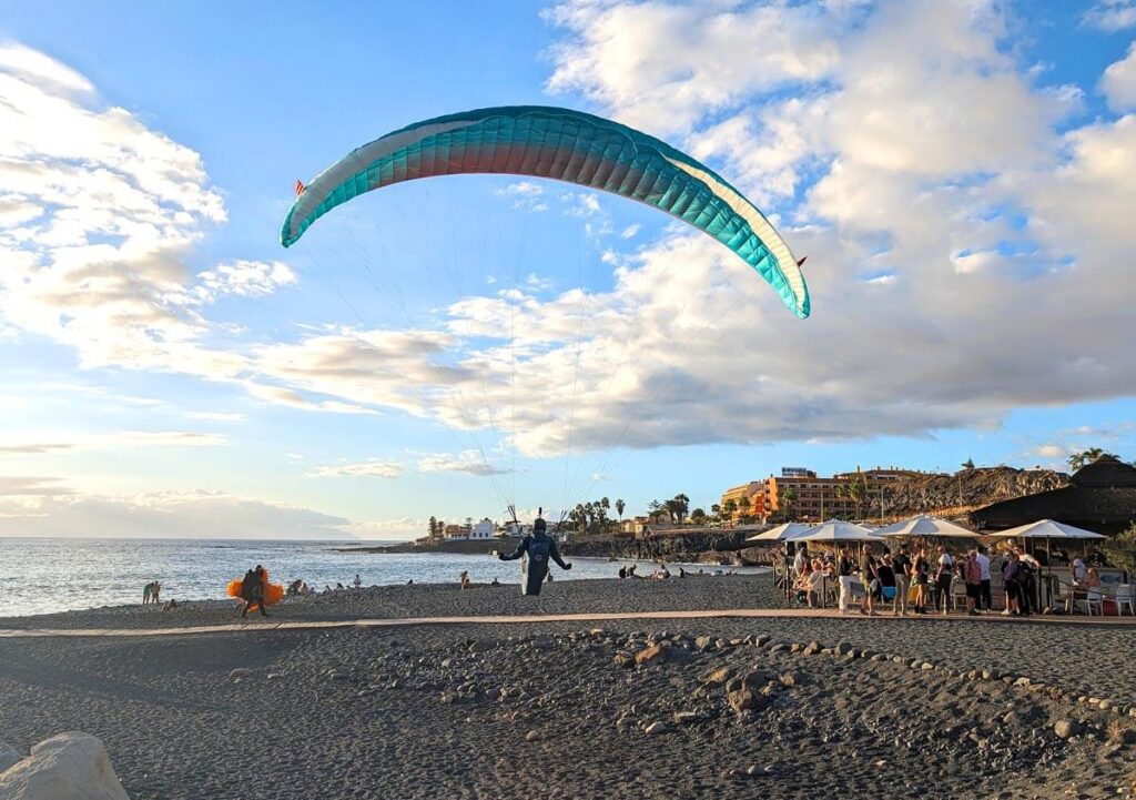 A paraglider landing on Playa de la Enramada in front of a beach bar