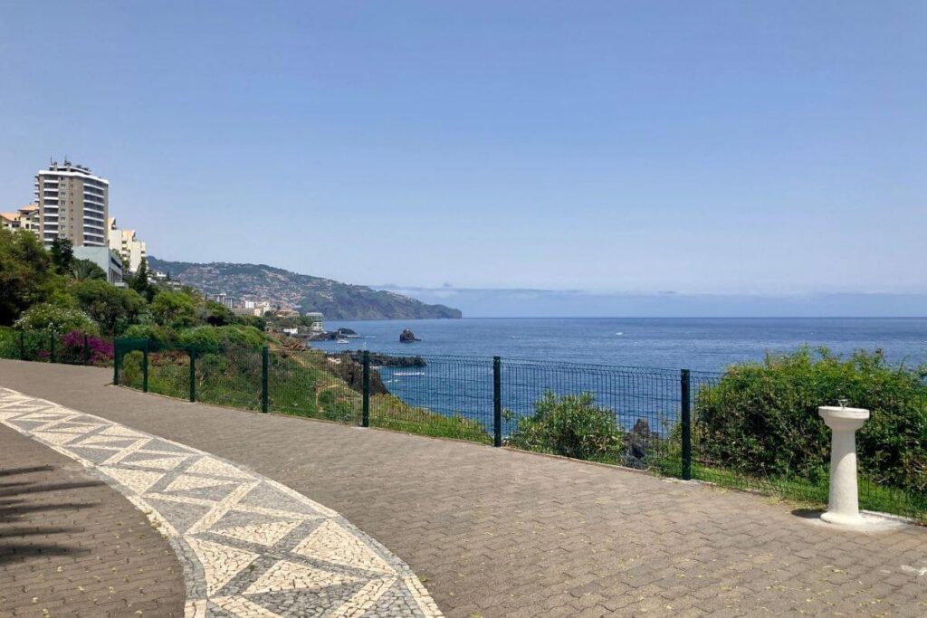 A wide, paved path along the coast, with blue skies