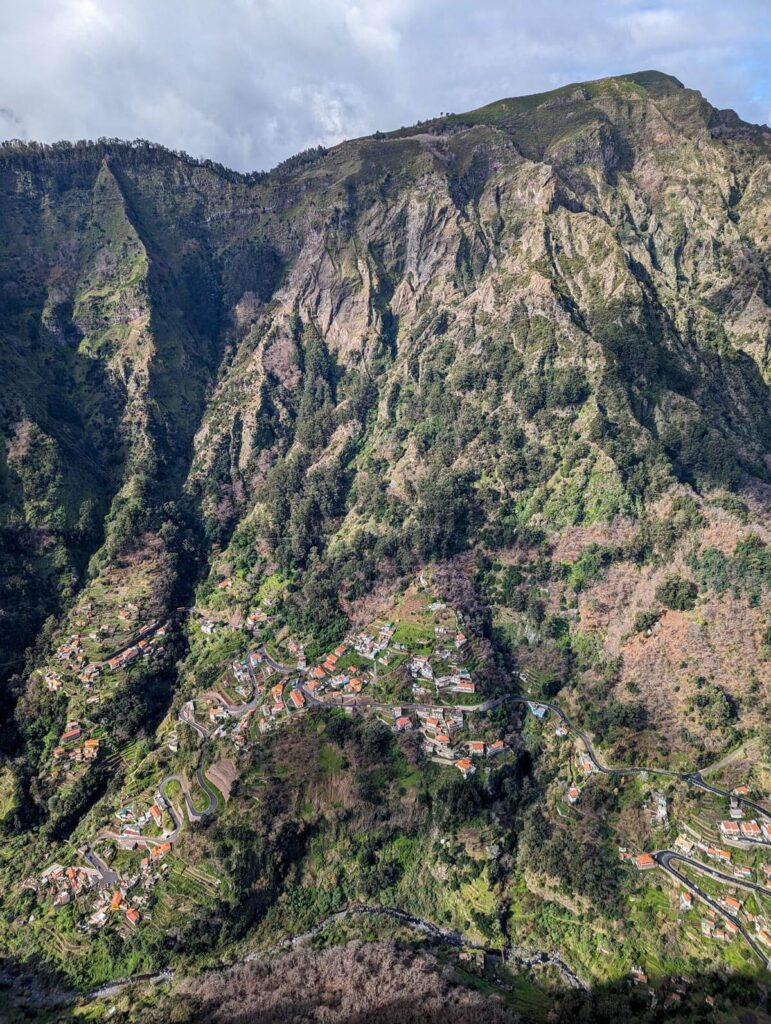 A view of the mountain side, with a village at the bottom. There's a winding road at the bottom of the mountain.