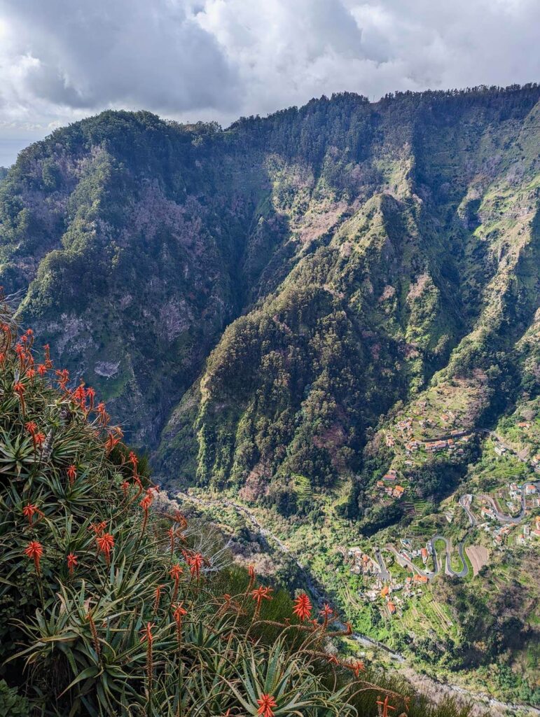 Spectacular mountain views at the Eira do Serrado viewpoint in Madeira. Green rocky mountain peaks descend into a valley far below. The houses in the valley look like miniature models.