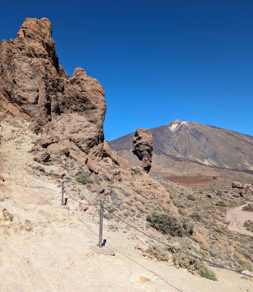 The Roques de Garcia rock formations in Teide National Park. Finger-like rocks stick up in the air against a bright blue sky with the peak of Mount Teide in the distance.