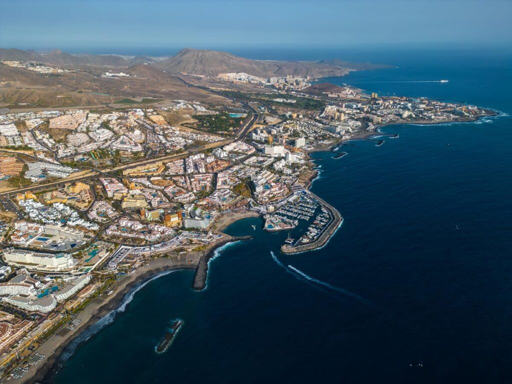 An aerial view of Costa Adeje. There are beaches all the way along the coastline, with hotels behind and rocky hills in the background. 