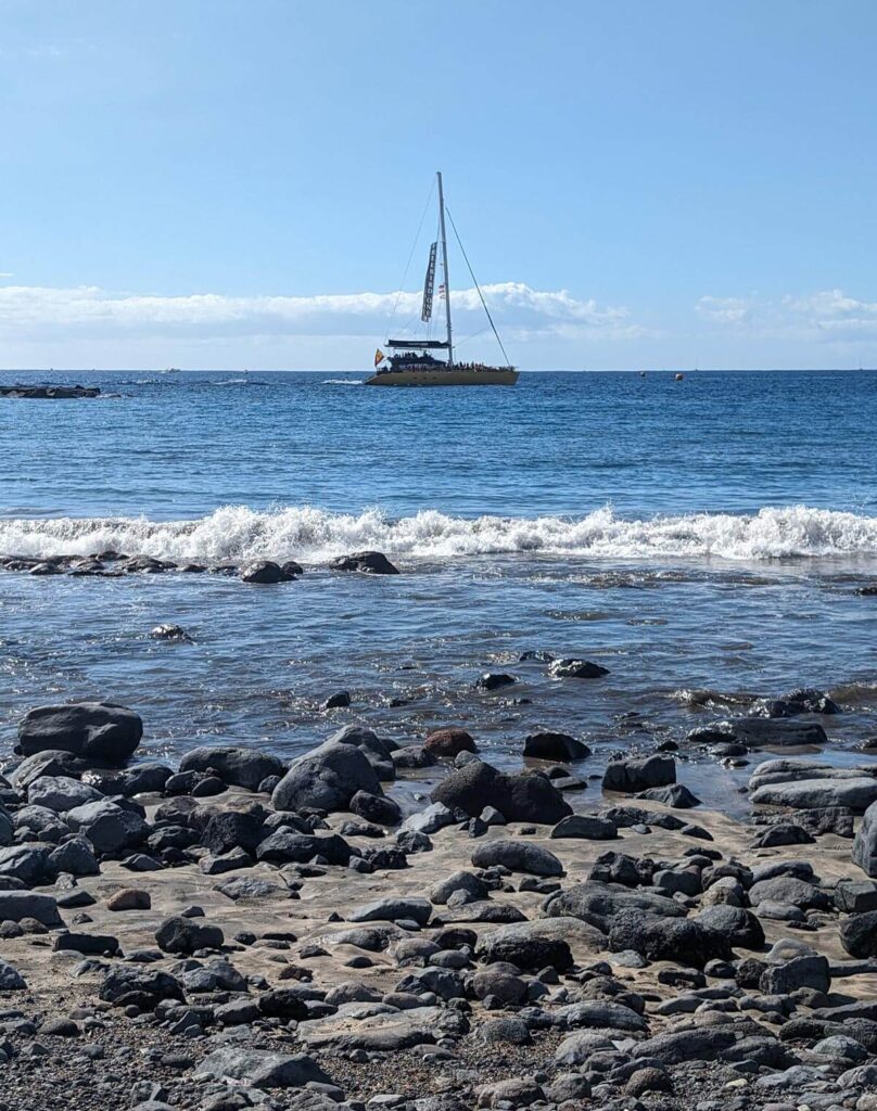 A boat passing a pebbly beach. Both the sky and the sea are blue.