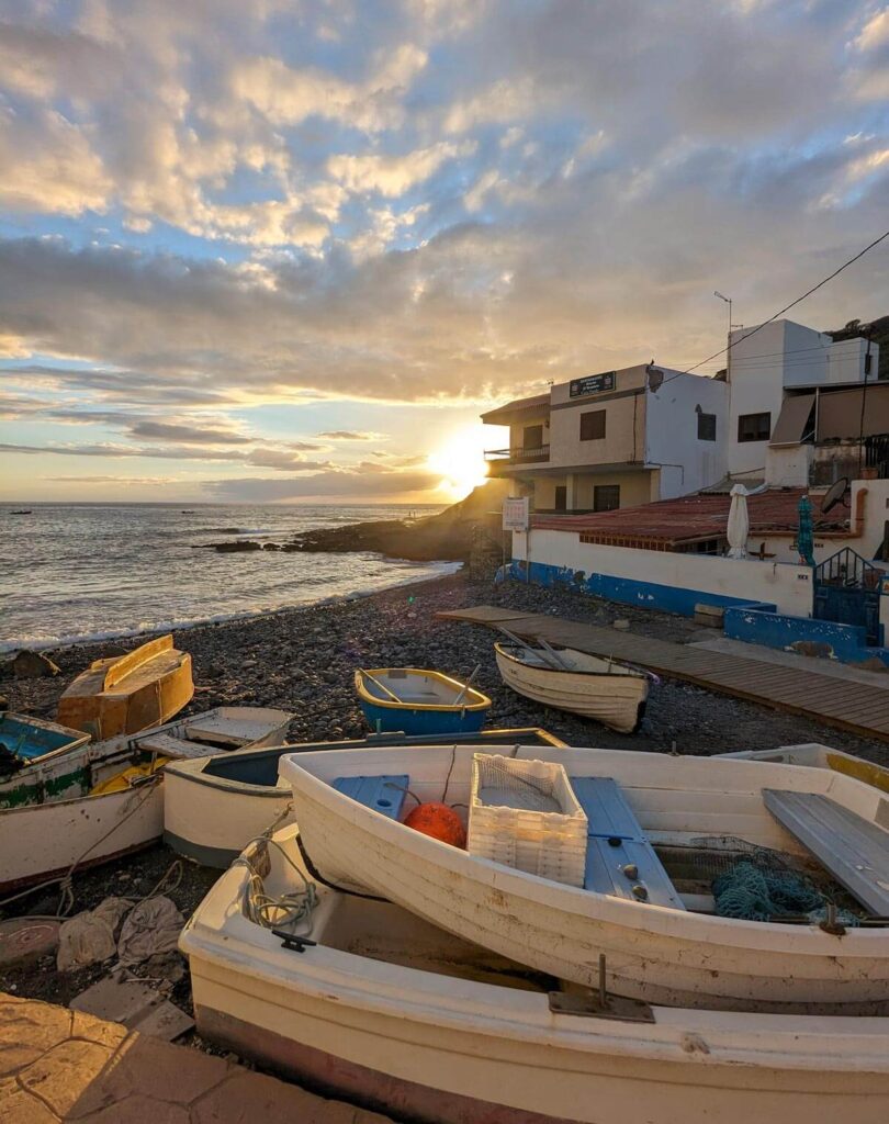 The small beach at La Caleta at sunset. Fishing boats are pulled up on the pebbly shore.