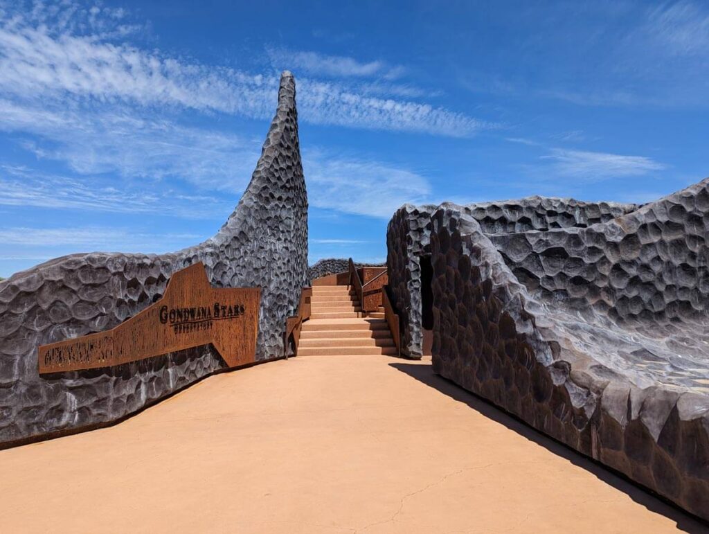 The entrance to Gondwana Stars Observatory in Outback Queensland. A wide sandy-coloured set of stairs are between dark grey low walls.