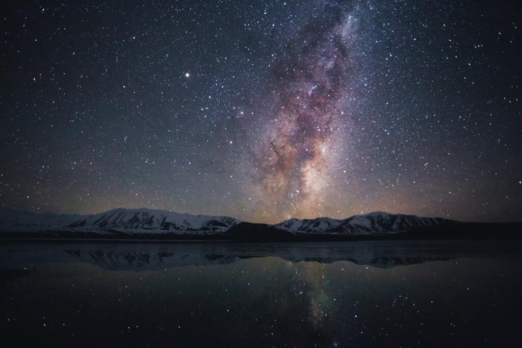 A magical view of the night sky reflected in Lake Tekapo, with mountains in the distance