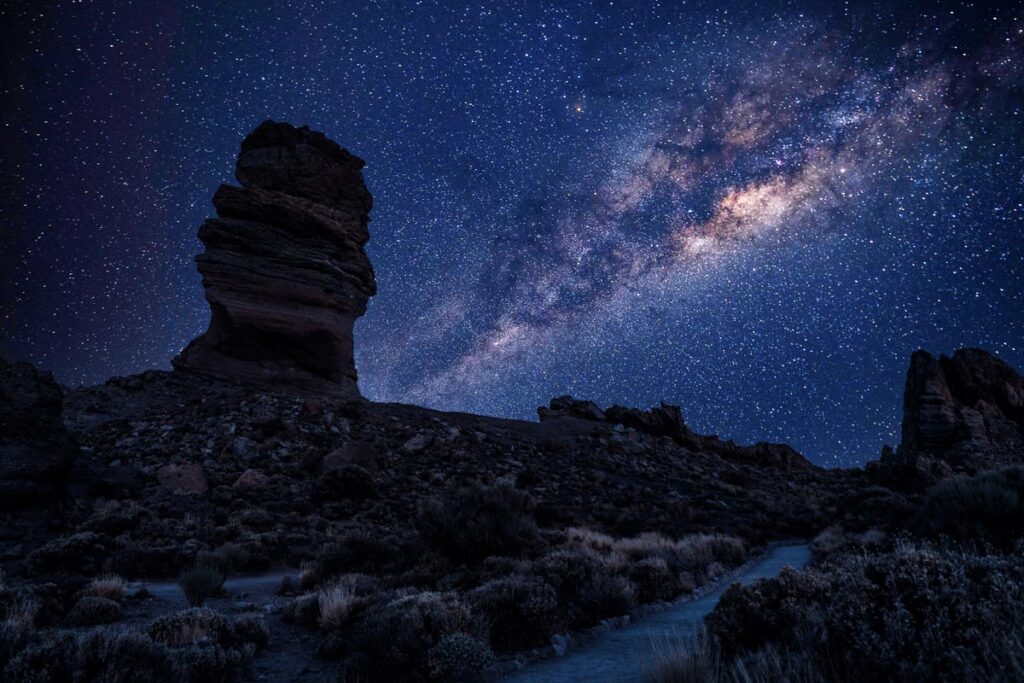 Stargazing on Mount Teide, Tenerife. A large rock formation points up into the sky, with stars and the Milky Way beyond