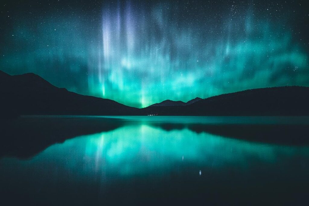 Bright green and blue northern lights reflecting in a lake in Jasper National Park