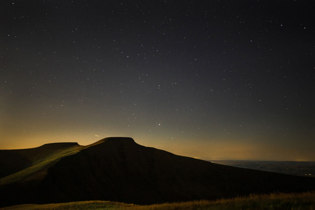 A dark night sky with stars above mountains in the Brecon Beacons, Wales