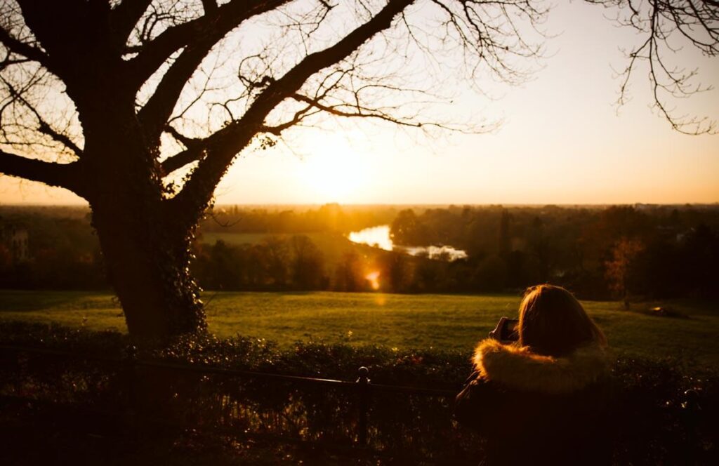 A sunset scene at King Henry's Mound in Richmond, London, with the evening sun glinting off the bend in the river Thames
