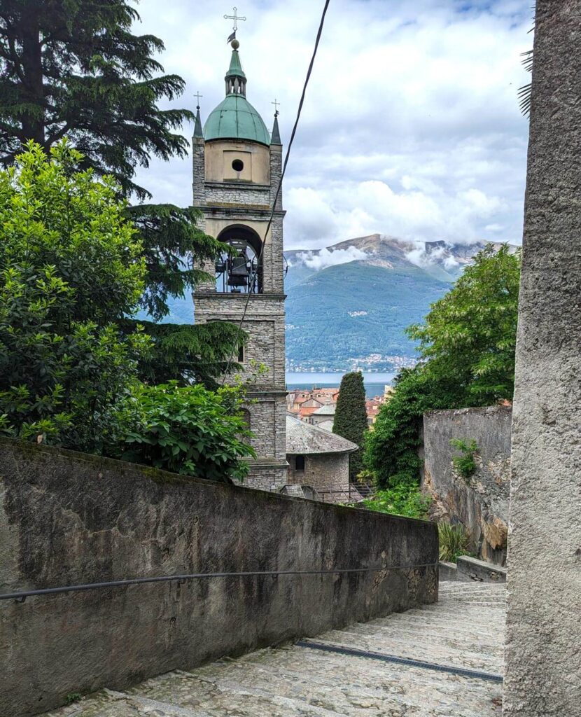 Stone steps leading down to a church with a tall tower, with a lake and mountains beyond