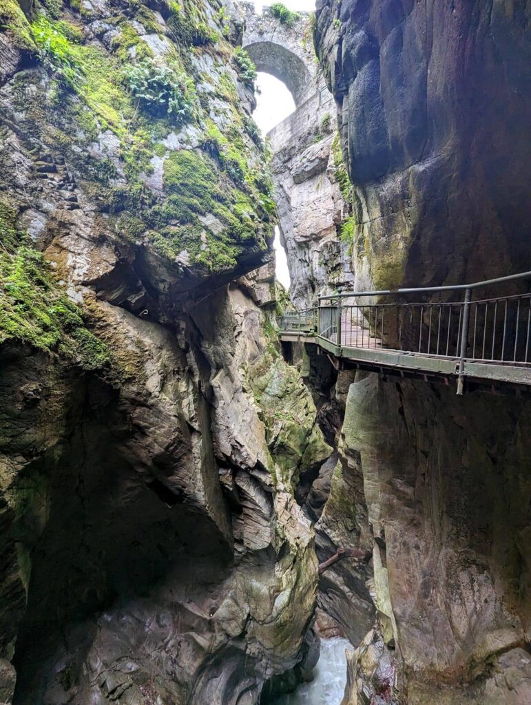 In a deep, rocky gorge, with a walkway on the right hand side and a river in the bottom. At the top of the picture, a stone bridge soars over it all.