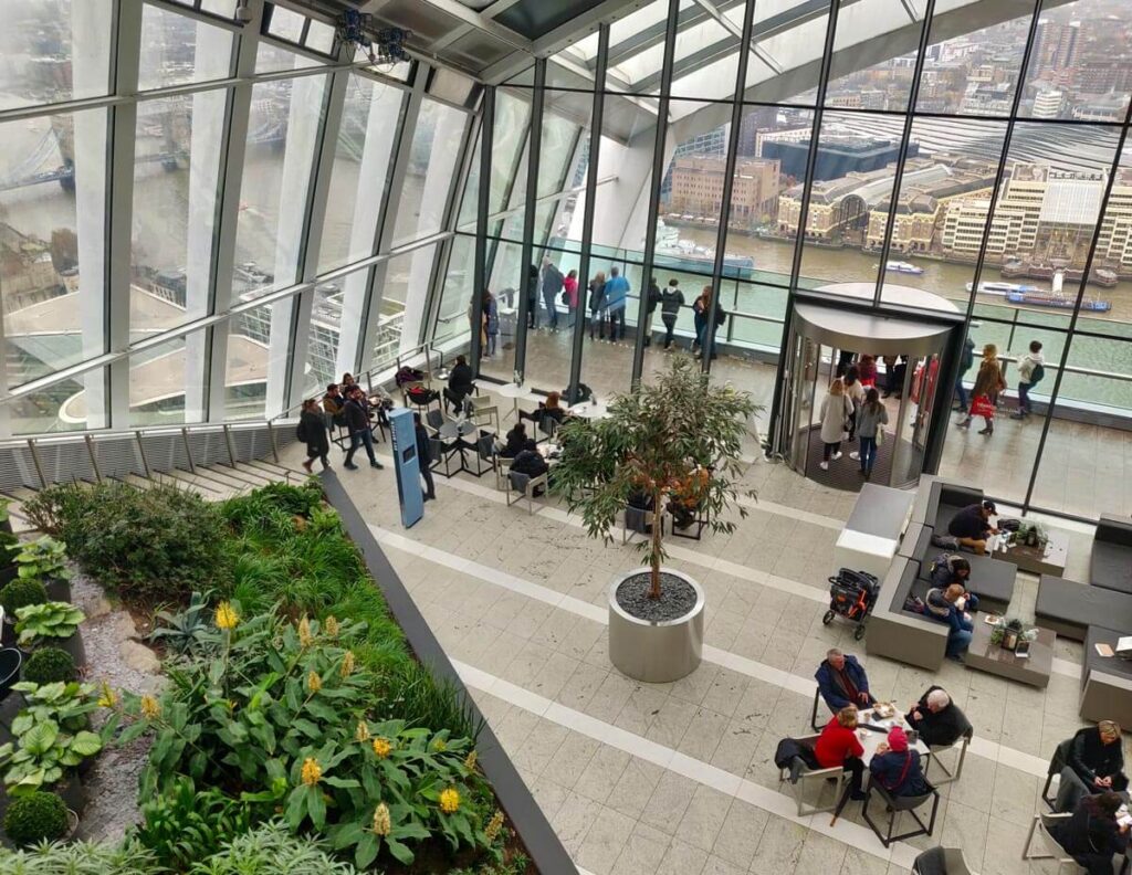 The Sky Garden at the top of the Walkie Talkie building. There is lush tropical planting with places to sit and large glass windows with views over the River Thames. A revolving door leads to the outdoor terrace.