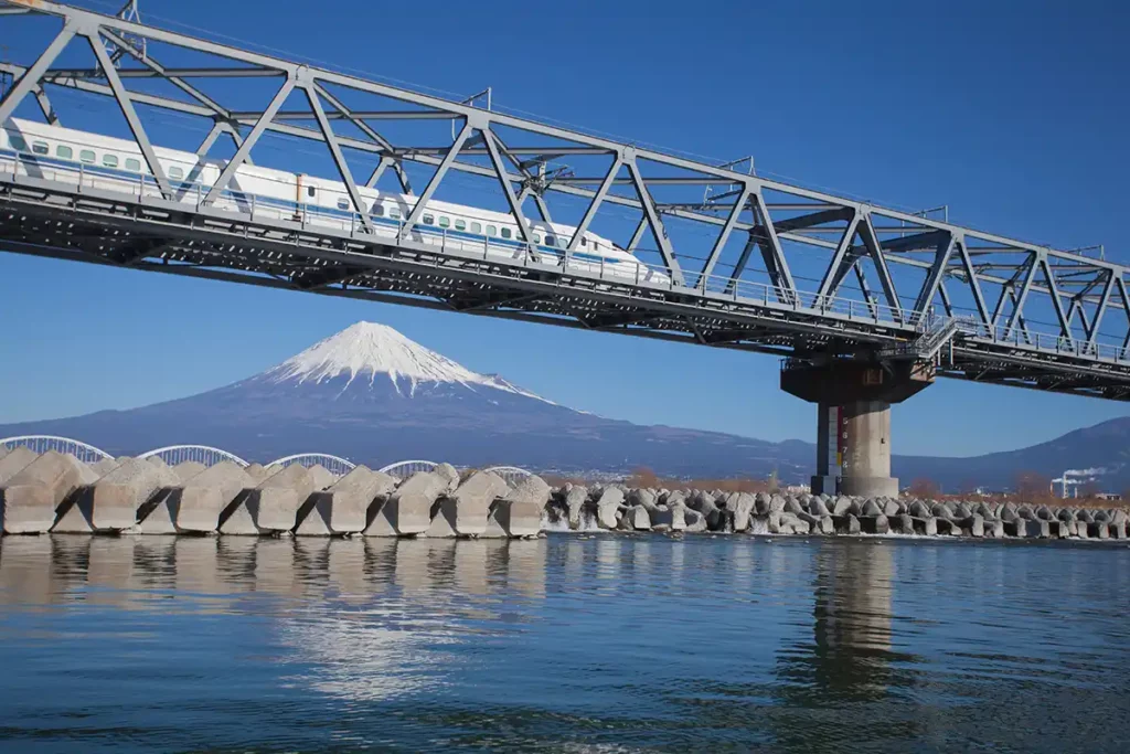 A bullet train crossing a bridge across a river, with Mount Fuji in the background