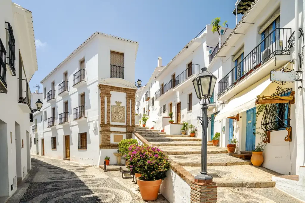 A pretty street in Frigiliana, with flowerpots and white houses underneath a blue sky