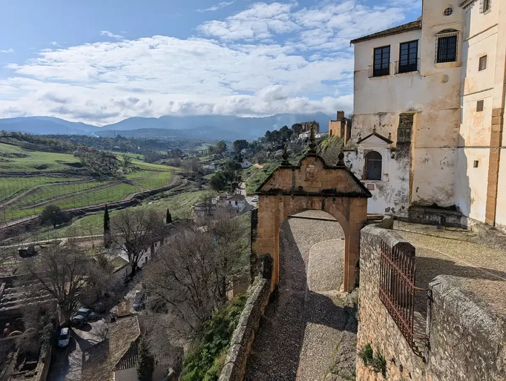 An old paved path underneath a beautiful arch, with the Andalucian countryside beyond